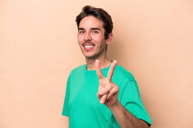 Beyazların arka planında izole edilmiş genç beyaz adam zafer işareti gösteriyor ve gülümsüyor..