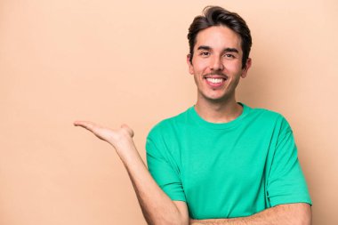 Beyaz, bej arka planda izole edilmiş genç bir adam bir avuç içinde fotokopi alanı ve belinde bir el daha gösteriyor..