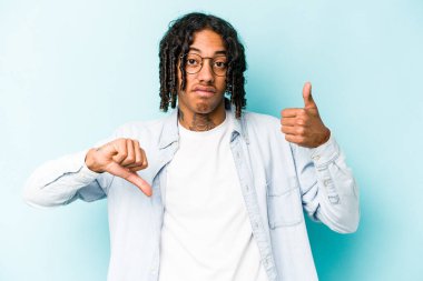 Genç Afro-Amerikalı adam mavi arka planda izole edilmiş, baş parmağını kaldırıyor, zor seçim konsepti