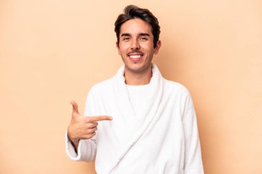 Beyaz bornoz giyen genç beyaz adam bej arka planda izole edilmiş gömlek fotokopi alanını gösteren, gururlu ve kendinden emin.
