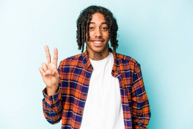 Genç Afrikalı Amerikalı adam mavi arka planda izole edilmiş neşeli ve kaygısız parmakları olan bir barış sembolü gösteriyor..