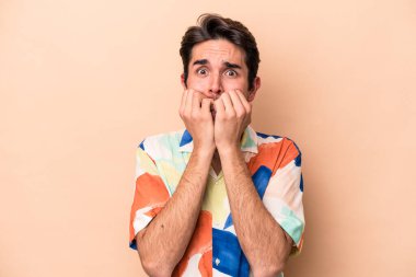 Beyazlı genç bir adam bej arka planda izole edilmiş tırnak yiyor, gergin ve endişeli..