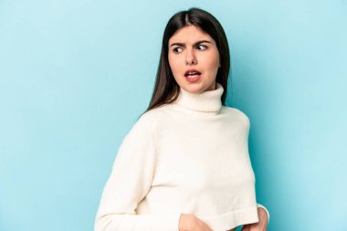 Mavi arka planda soyutlanmış genç beyaz kadın gülümseyen, neşeli ve keyifli bir tarafa bakıyor..