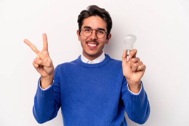 Beyaz arka planda izole edilmiş bir ampul tutan genç beyaz bir adam neşeli ve kaygısız parmakları olan bir barış sembolü gösteriyor..