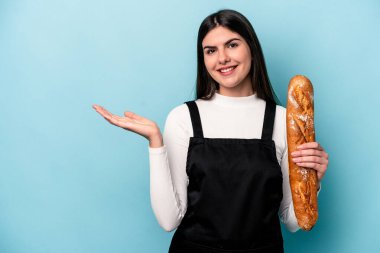 Genç fırıncı beyaz elinde mavi arka planda izole edilmiş bir somun ekmek tutarken bir avuç içinde fotokopi alanı ve belinde bir el daha gösteriyor..