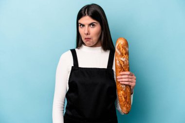 Genç fırıncı Kafkas elinde mavi arka planda izole edilmiş bir somun ekmek omuz silker ve kafası karışmış gözler.