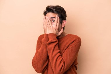 Beyazlı genç bir adam bej arka planda izole edilmiş. Korkmuş ve gergin parmaklarıyla göz kırp..