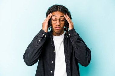 Genç Afrikalı Amerikalı adam mavi arka planda izole edilmiş tapınaklara dokunuyor ve baş ağrısı çekiyor..