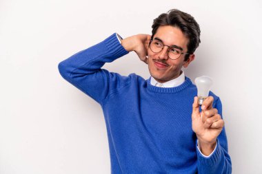 Beyaz arka planda izole edilmiş bir ampul tutan genç beyaz bir adam kafasının arkasına dokunuyor, düşünüyor ve bir seçim yapıyor..