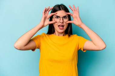 Mavi arka planda izole edilmiş genç beyaz kadın bir başarı fırsatı bulmak için gözlerini açık tutuyor..