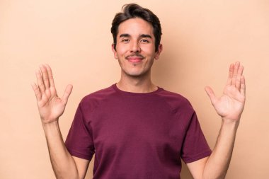 Beyaz tenli genç adam bej arka planda izole edilmiş. Elinde parmakları olan, gülümseyen ve kendinden emin bir şey var..