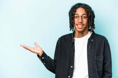 Mavi arka planda izole edilmiş genç Afrikalı Amerikalı bir adam bir avuç içinde fotokopi alanı ve belinde bir el daha gösteriyor..