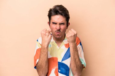 Beyazlı genç bir adam bej arka planda izole edilmiş, yumruğunu kameraya gösteriyor, agresif yüz ifadesi var..