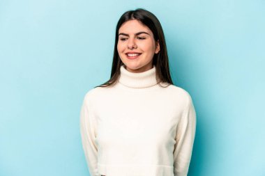 Mavi arka planda izole edilmiş genç beyaz kadın gülüyor ve gözlerini kapıyor, rahatlamış ve mutlu hissediyor..