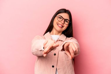 Pembe arka planda izole edilmiş genç beyaz kadın parmaklarıyla ön tarafı işaret ediyor..