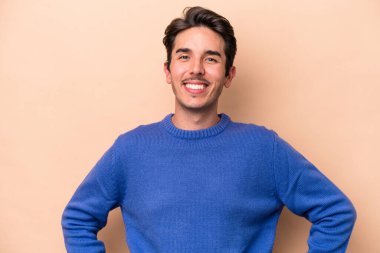 Beyaz tenli genç adam bej arka planda izole edilmiş. Kendine güveniyor. Kalçaları tutuyor..