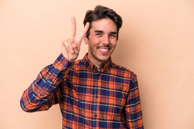 Beyazlı genç bir adam bej arka planda izole edilmiş. İki numarayı parmaklarıyla gösteriyor..