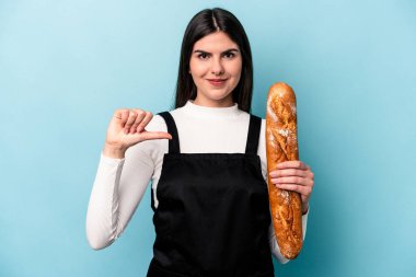 Mavi arka planda izole edilmiş bir somun ekmek tutan genç bir fırıncı gururlu ve kendinden emin hissediyor, örnek olarak.