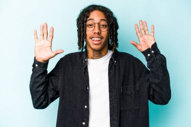 Genç Afrikalı Amerikalı bir adam mavi arka planda izole edilmiş. Hoş bir sürpriz, heyecanlı ve el kaldırıyor..