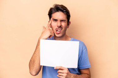 Beyazlı genç bir adam bej arka planda izole edilmiş bir pankart tutuyor işaret parmağıyla hayal kırıklığı jesti gösteriyor..