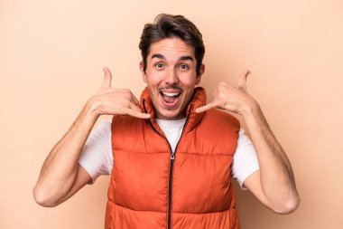 Beyazlı genç bir adam bej arka planda izole edilmiş. Cep telefonu hareketini parmaklarıyla gösteriyor..