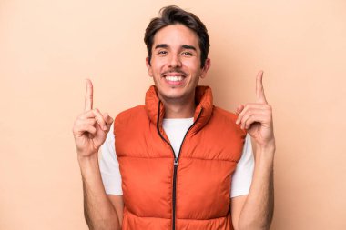 Beyazlı genç bir adam bej arka planda izole edilmiş iki parmağı da boş bir alan gösteriyor..