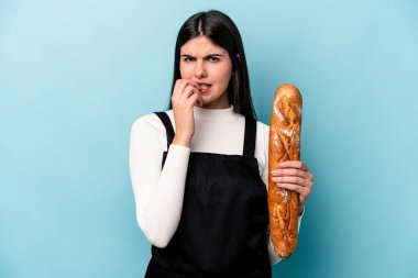 Genç fırıncı Kafkas elinde mavi arka planda izole edilmiş bir somun ekmek tutuyor tırnaklarını yiyor, gergin ve çok endişeli..