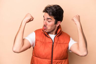 Beyaz tenli genç adam bej arka planda izole edilmiş. Güçlü bir hareket sergiliyor. Kadın gücünün sembolü.