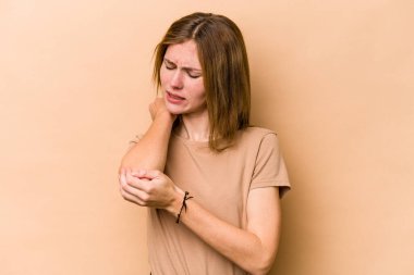 Genç İngiliz kadın bej arka planda izole edilmiş. Dirsek masajı yapıyor. Kötü bir hareketin ardından acı çekiyor..