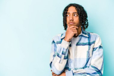 Genç Afrikalı Amerikalı bir adam mavi arka planda izole edilmiş şüpheli ve şüpheci bir ifadeyle yana bakıyor..