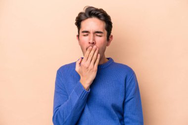 Beyazlı genç bir adam bej arka planda izole edilmiş esniyor. Ağzı eliyle kapatan yorgun bir hareket sergiliyor..