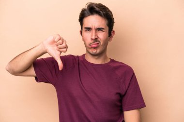 Beyazlı genç adam bej arka planda izole edilmiş baş parmağını aşağı gösteren, hayal kırıklığı konsepti.