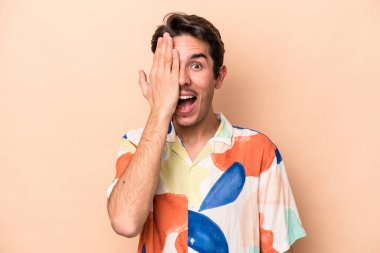 Beyaz tenli genç adam bej arka planda izole edilmiş. Yüzünün yarısını palmiye ile örterek eğleniyor..