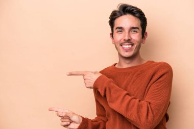 Beyazlı genç adam bej arka planda izole edilmiş. İşaret parmaklarıyla işaret ettiği için heyecanlı..
