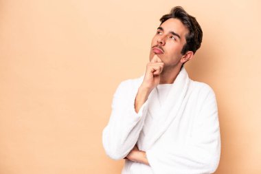 Kafkasyalı genç bir adam bej arka planda izole edilmiş şüpheli ve şüpheci bir ifadeyle yana bakıyor..