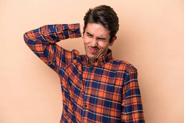 Beyazlı genç bir adam bej arka planda izole edilmiş. Yorgun ve uykulu. Elini başının üstünde tutuyor..