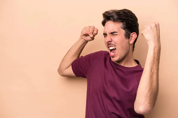 Ung Kaukasier Man Isolerad Beige Bakgrund Höja Näve Efter Seger — Stockfoto