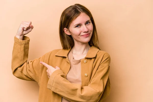 Young English woman isolated on beige background showing strength gesture with arms, symbol of feminine power