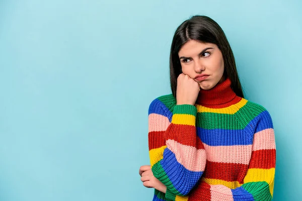 Mavi arka planda izole edilmiş, üzgün ve dalgın hisseden, kopyalama alanına bakan beyaz bir kadın..