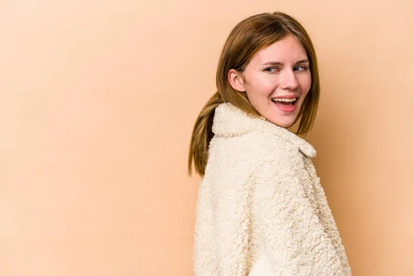 Young English woman isolated on beige background looks aside smiling, cheerful and pleasant.