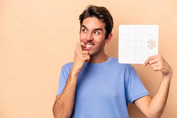 Jonge Blanke Man Met Een Puzzel Geïsoleerd Beige Achtergrond Ontspannen — Stockfoto