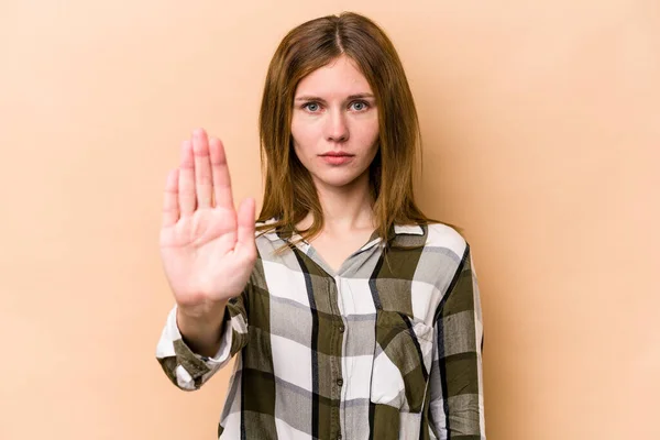 Young English woman isolated on beige background standing with outstretched hand showing stop sign, preventing you.