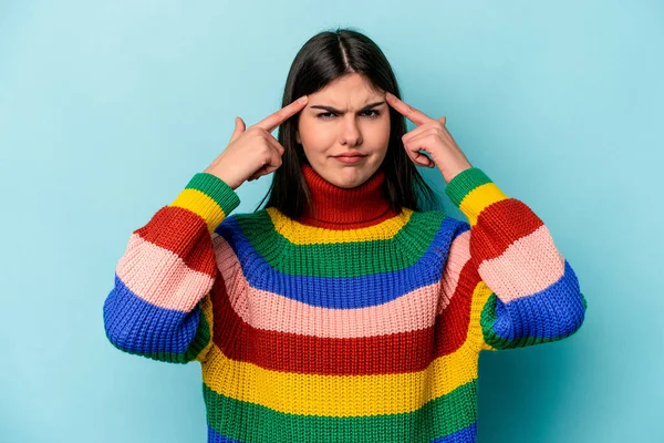 Kafkasyalı genç bir kadın mavi arka planda izole edilmiş bir vazifeye odaklanmış, parmaklarını işaret ediyor..