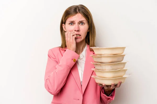Young business English woman holding tupperware of food isolated on white background biting fingernails, nervous and very anxious.