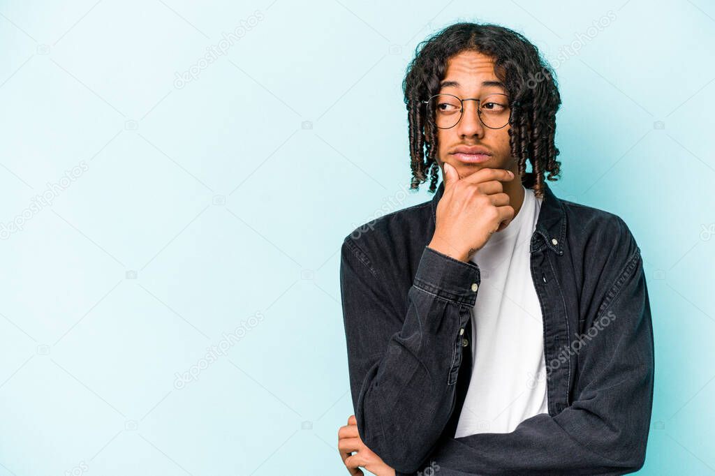Young African American man isolated on blue background relaxed thinking about something looking at a copy space.