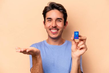 Beyazlı genç bir adam bej arka planda izole edilmiş bir bateriyi tutuyor bir avuç içinde fotokopi alanı ve belinde başka bir el tutuyor..