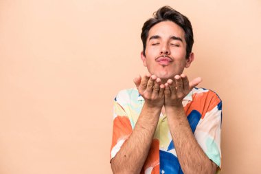 Beyaz tenli genç adam bej arka planda izole edilmiş dudaklar kıvrılmış ve hava öpücüğü göndermek için avuç içleri tutulmuş..