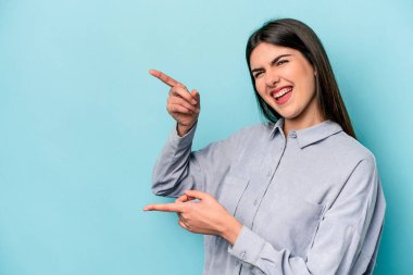 Mavi arka planda izole edilmiş genç beyaz kadın işaret parmağıyla işaret ederek heyecanlanıyor..