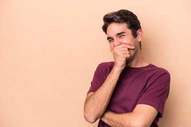 Beyaz tenli genç adam bej arka planda izole edilmiş gülerek, kaygısız, doğal duygularla gülüyor..