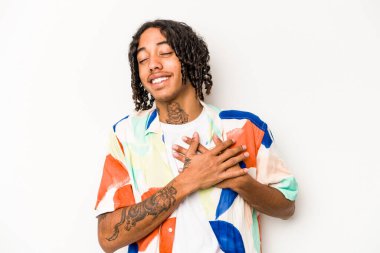 Genç Afrikalı Amerikalı adam beyaz arka planda soyutlanmış gülüyor, ellerini yüreğine koyuyor, mutluluk kavramını koruyor..